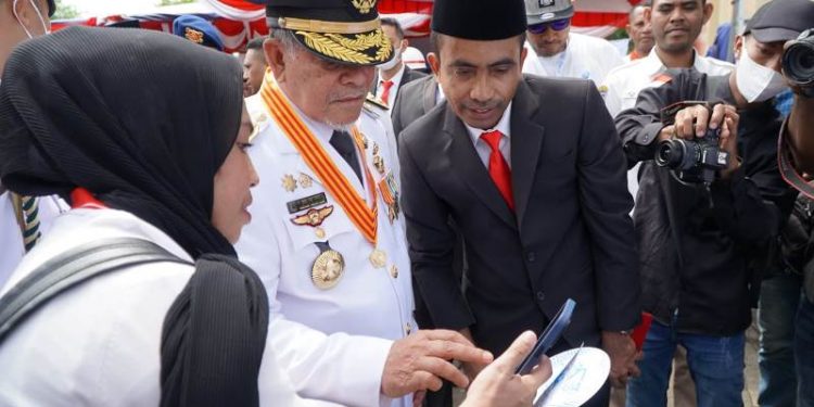 Kadisarpus Malut Muliadi (jas hitam) menunjukan Aplikasi gagasan SIBUA Literasi pada Gubernur Malut KH Abdul Gani Kasuba. (Foto : Disarpus Malut)